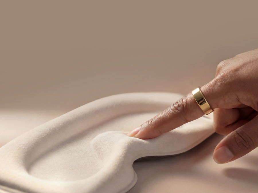 Hand with a gold ring touching a smooth, beige surface